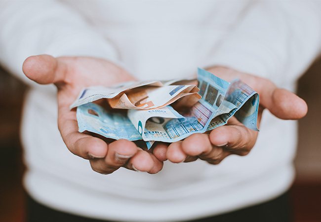 Eine Person hält mit beiden Händen Geldscheine in die Kamera. Sie konnte nach einem Internetbetrug erfolgreich das Geld zurückfordern. Bild: Unsplash/Christian Dubovan